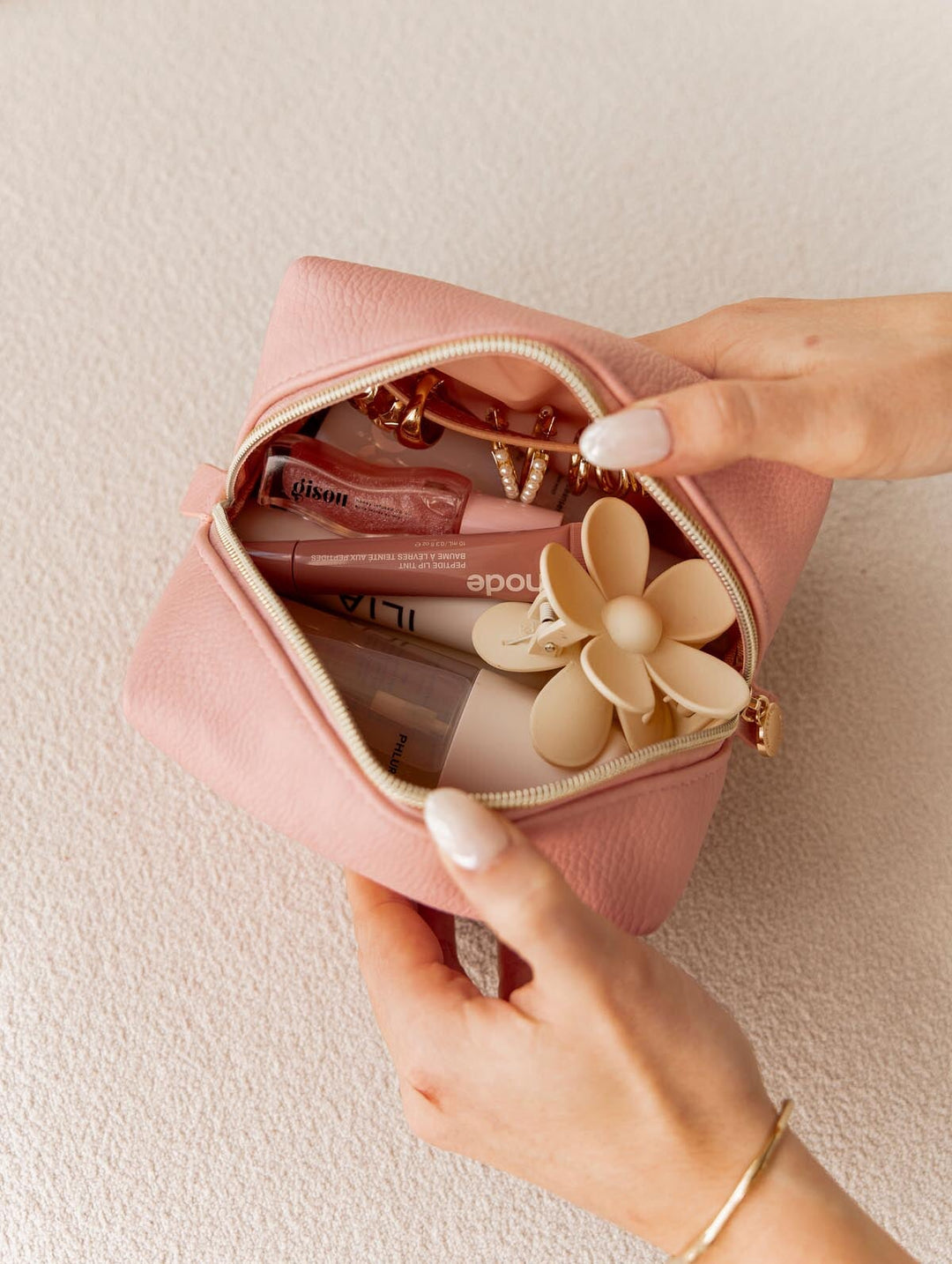 Pink makeup bag held open against a beige background