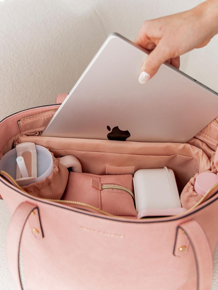 Hand removing a laptop from a pink tote bag
