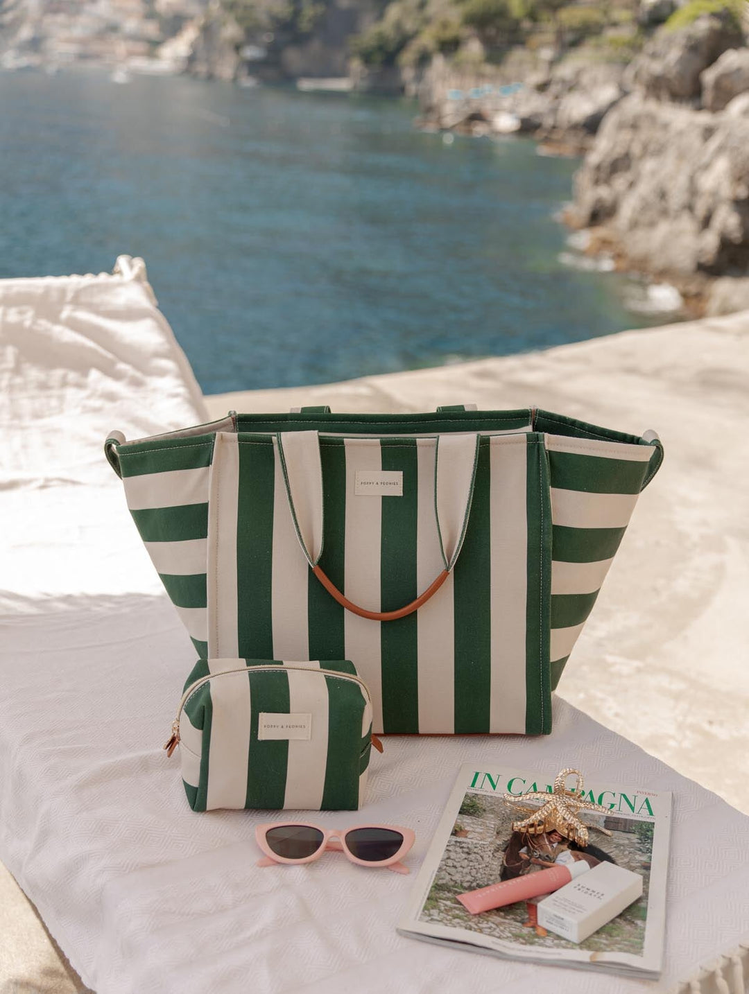 Green and white striped tote bag with matching cosmetic bag on a chair overlooking a scenic view.