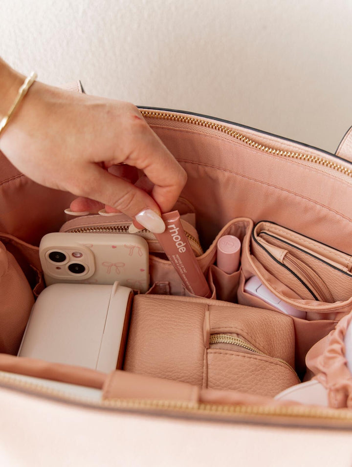 Hand pulling a lip balm out of a pink tote bag