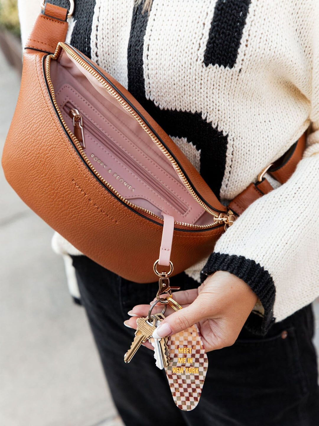 Person holding a brown vegan leather bag with a keychain and checkered charm.