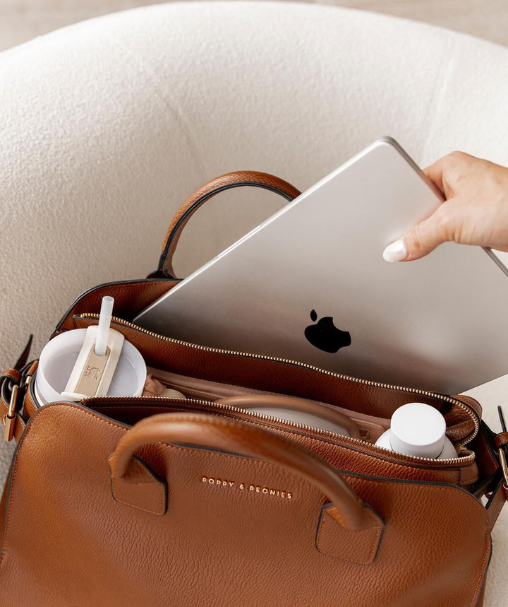 Hand placing a laptop into a brown vegan leather tote bag