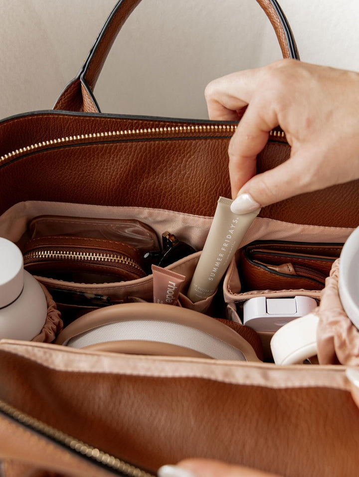 Person pulling lip gloss out of a vegan leather handbag