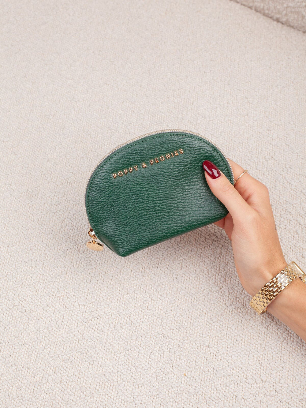 Product-focused lifestyle shot of the Knot Today Jewelry Case in Heritage Green, showcasing its compact rounded silhouette, textured exterior, and gold-tone branding.