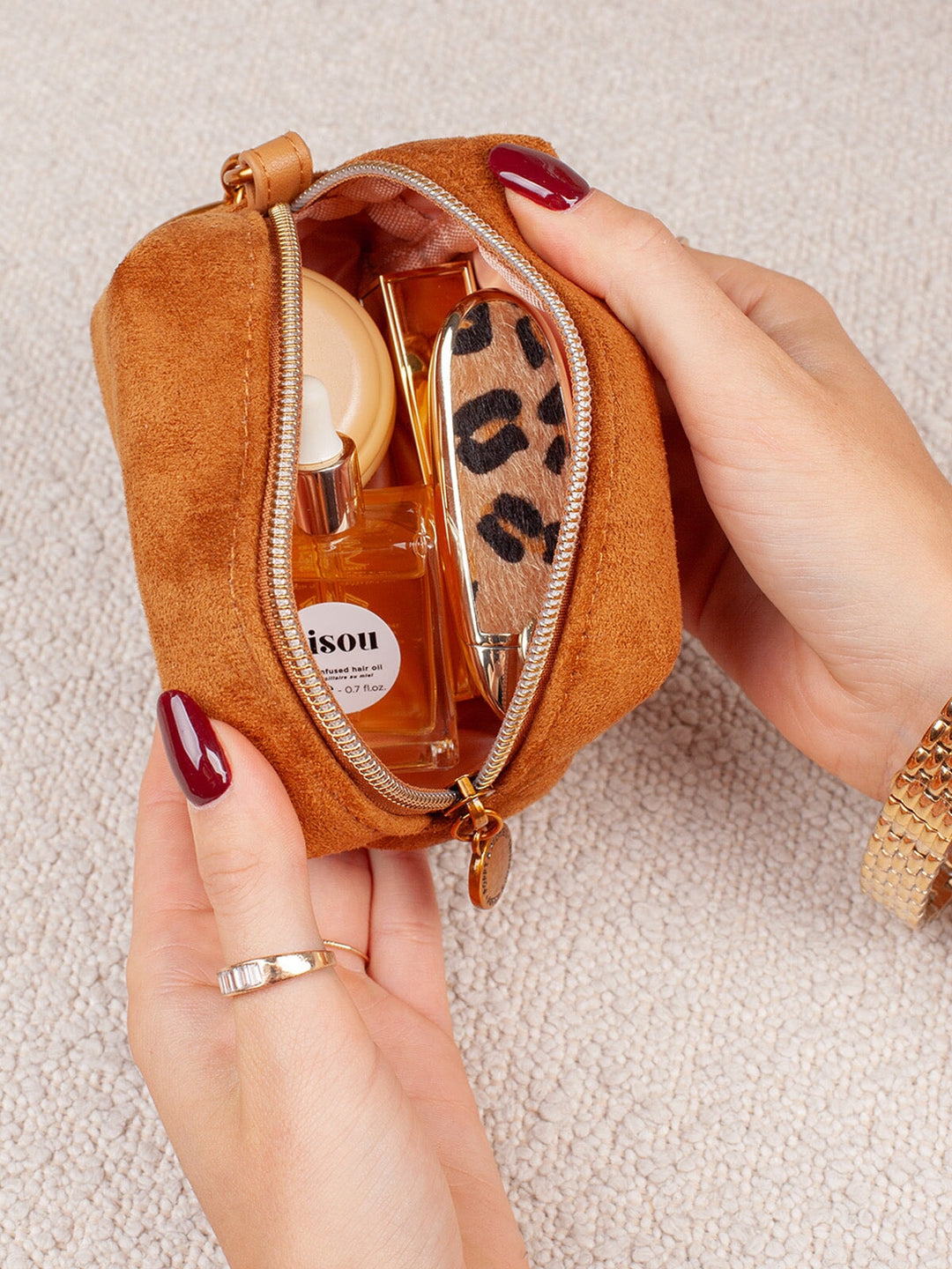 Open view of Poppy & Peonies Tag Along Charm in Cognac Suede, showing the compact zippered case holding small beauty essentials with gold-tone hardware.