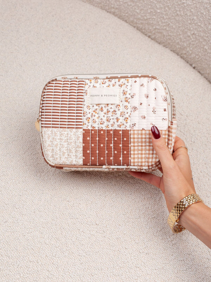 Handheld lifestyle shot of the Poppy & Peonies Pretty Connected Case in Brown Patchwork, showcasing its quilted patchwork exterior, compact structured shape, and double-zip design.