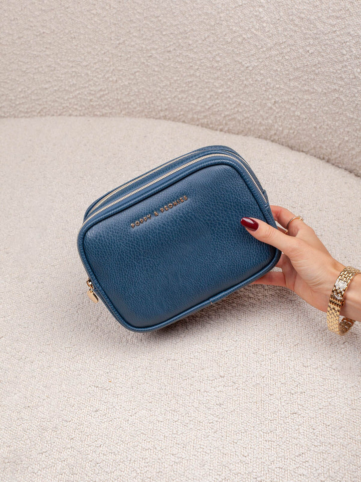 Handheld lifestyle shot of the Poppy & Peonies Pretty Connected Case in Navy, showcasing its rich navy exterior, compact structured silhouette, double-zip design, and gold-tone branding.