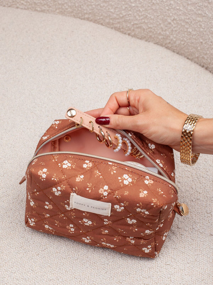 Product-focused lifestyle shot of the Cosmetic Trio in Brown Patchwork, highlighting the brown floral cosmetic case with its structured shape and zip-around closure.