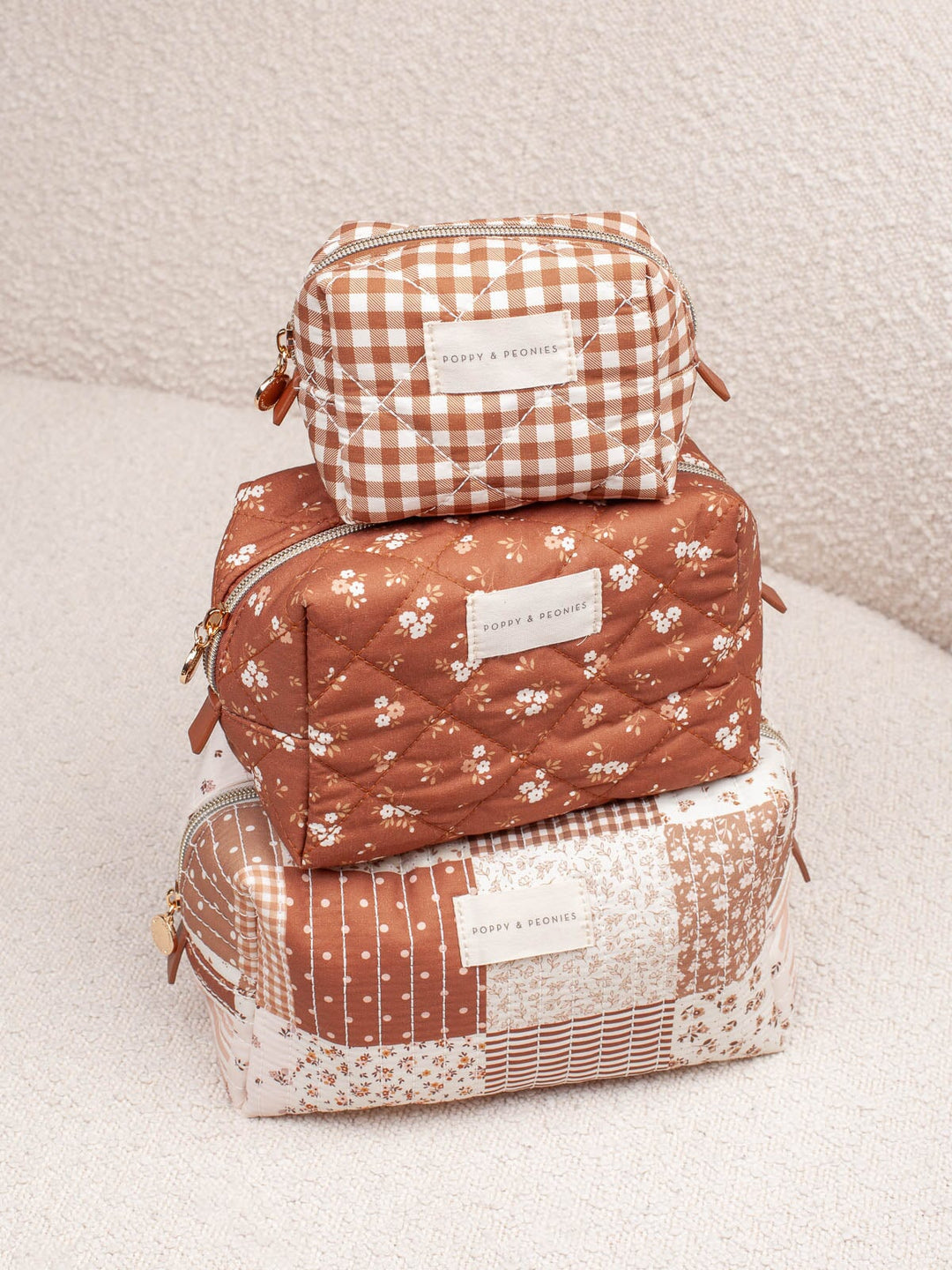 Product-focused lifestyle shot of the Cosmetic Trio in Brown Patchwork, featuring all three coordinating cosmetic cases stacked together.