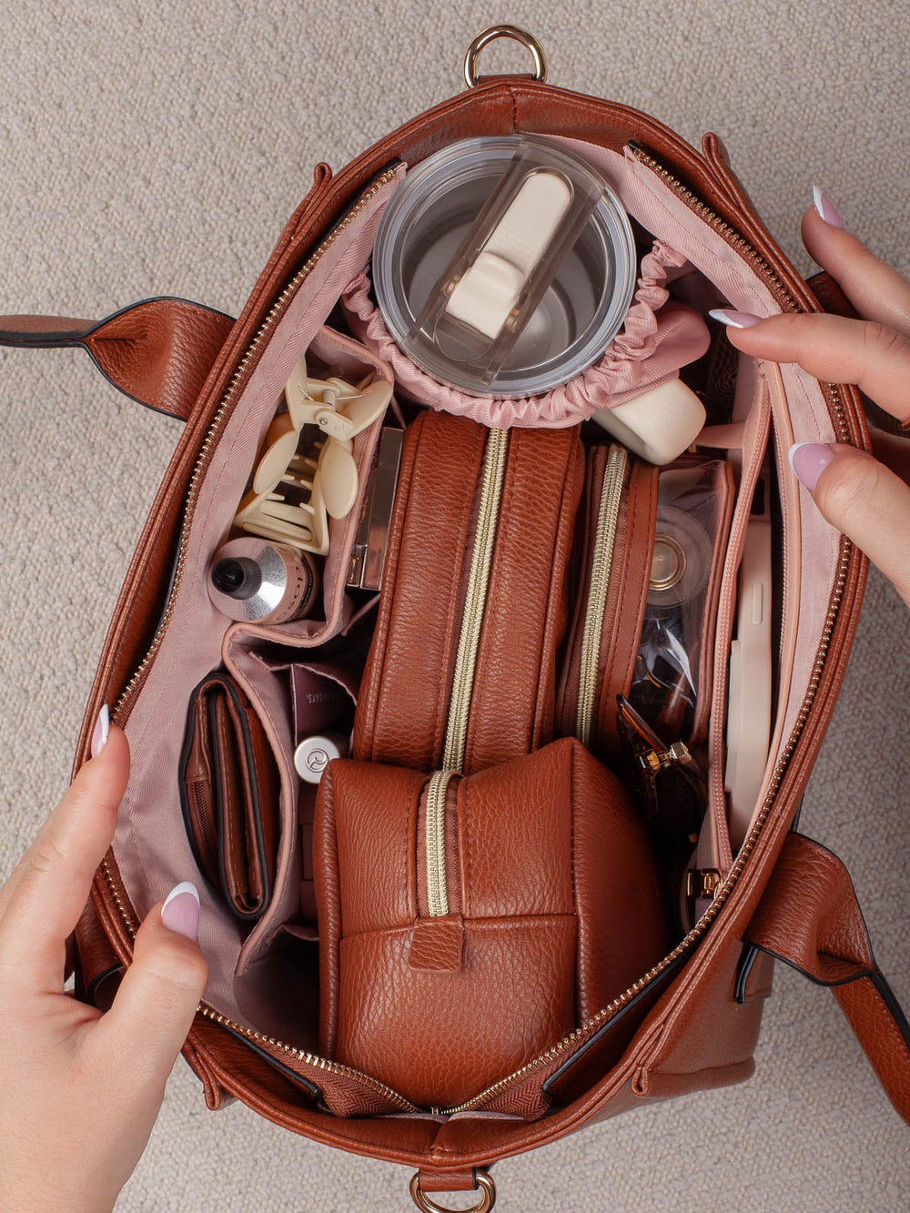 Overhead lifestyle shot of the Small Multitasker in Chestnut, showcasing its spacious organized interior with cosmetic cases, a tumbler, and everyday essentials.