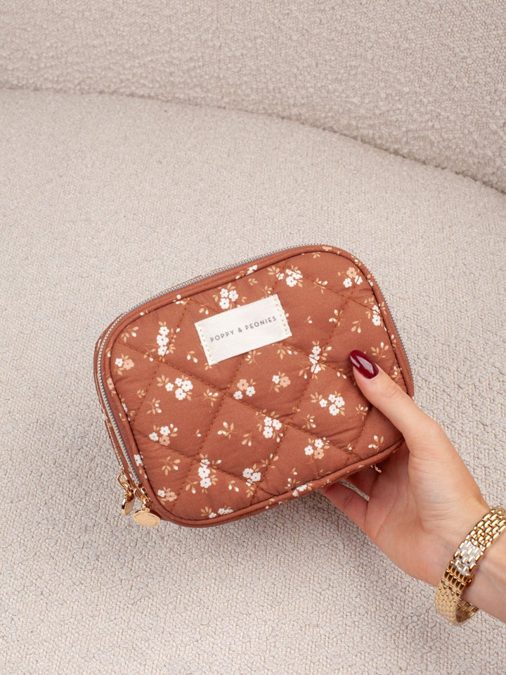 Handheld lifestyle shot of the Poppy & Peonies Pretty Connected Case in Brown Floral, highlighting its compact size, quilted texture, and floral print.