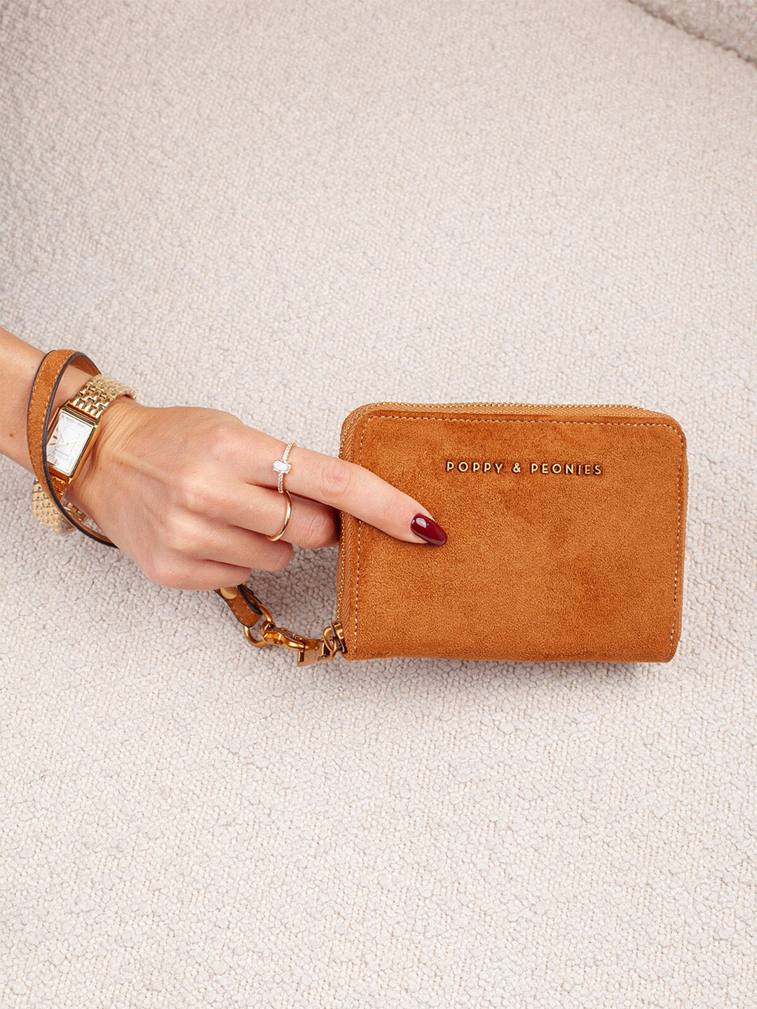 Poppy & Peonies The Grab and Go Wallet in Cognac Suede held in hand, showcasing its compact size, soft suede exterior and detachable wrist strap.