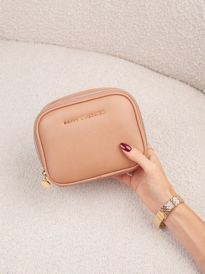 Handheld lifestyle shot of the Poppy & Peonies Pretty Connected Case in Taupe, showcasing its rich taupe exterior, compact structured silhouette, double-zip design, and gold-tone branding.