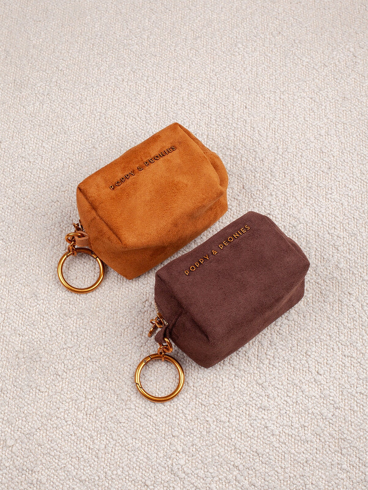 Poppy & Peonies Tag Along Charms in Cognac Suede and Espresso Suede displayed together, featuring compact zippered cases with gold-tone key rings.