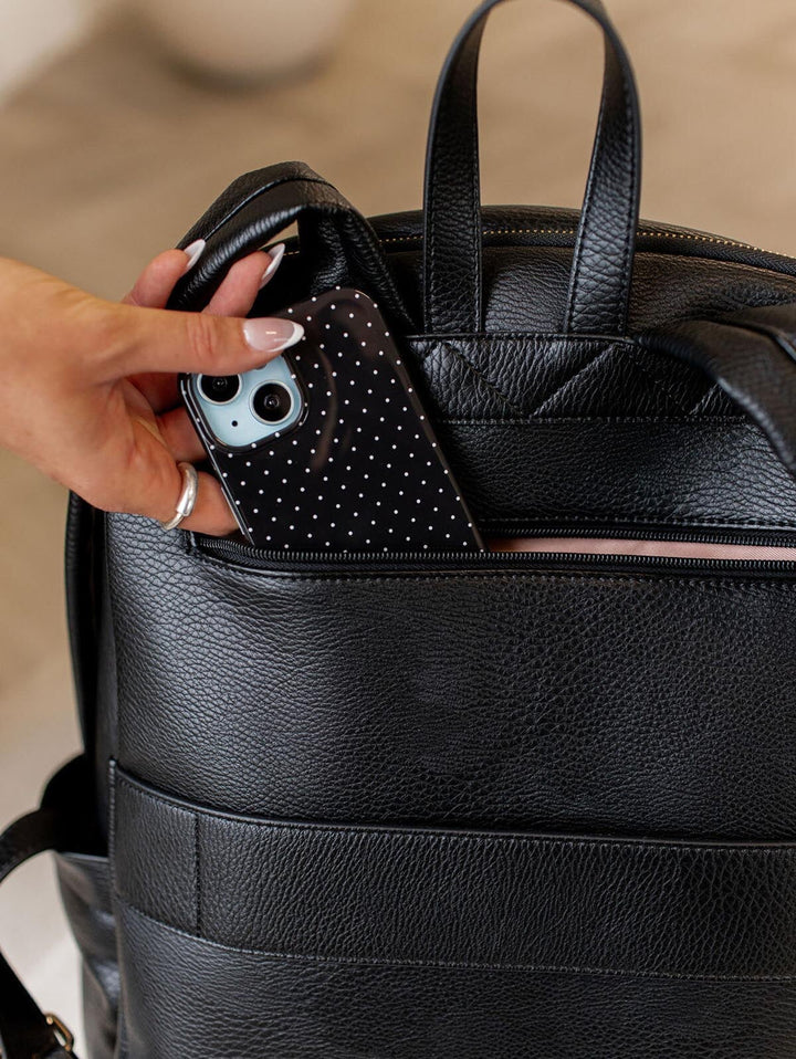 Person placing a black polka dot phone case into a black vegan leather backpack.