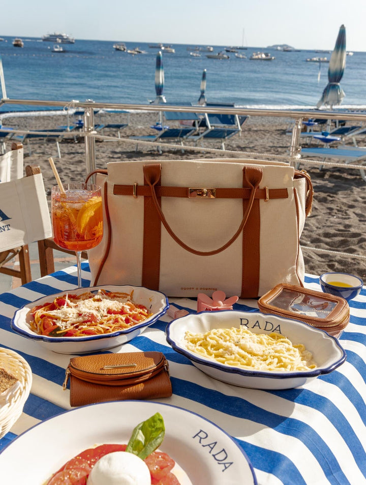 Table with Italian food and drinks by the beach, featuring a white and brown bag.