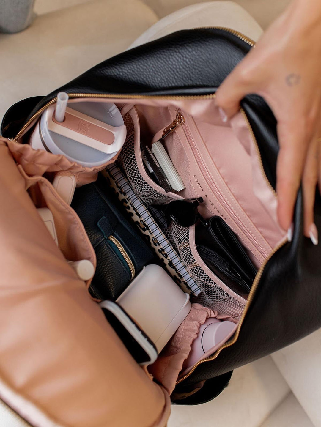 Person opening a black vegan leather backpack with various items inside.