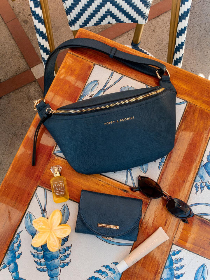 Navy blue handbag, a bottle of perfume, sunglasses, and a hair clip on a table