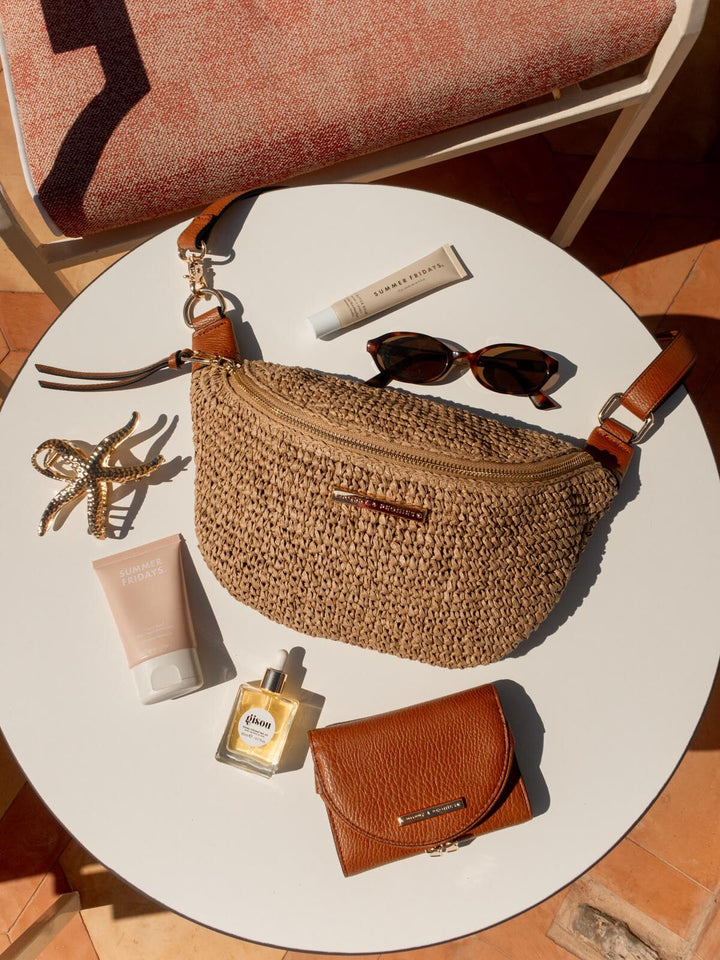 Raffia straw bag, sunglasses, and other accessories on a round white table.