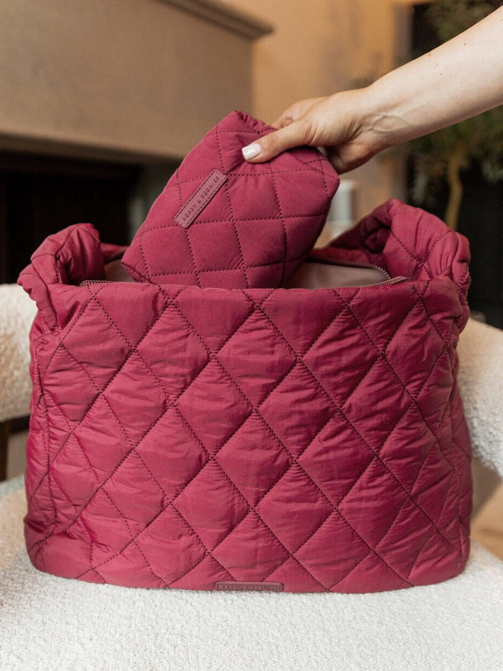 Person putting a makeup bag into a quilted berry coloured hobo bag