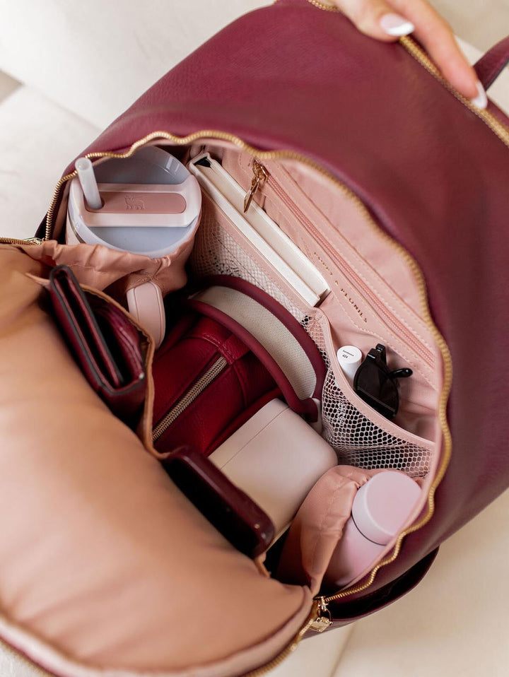 Open berry coloured backpack with various items including a Stanley water bottle.