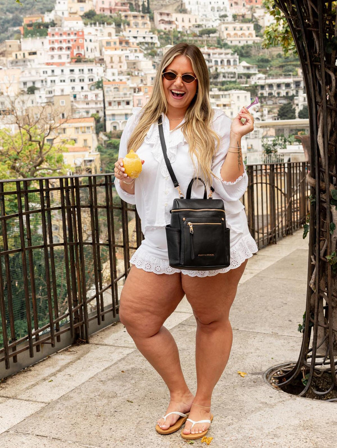 Woman in white outfit with black backpack standing on a scenic overlook