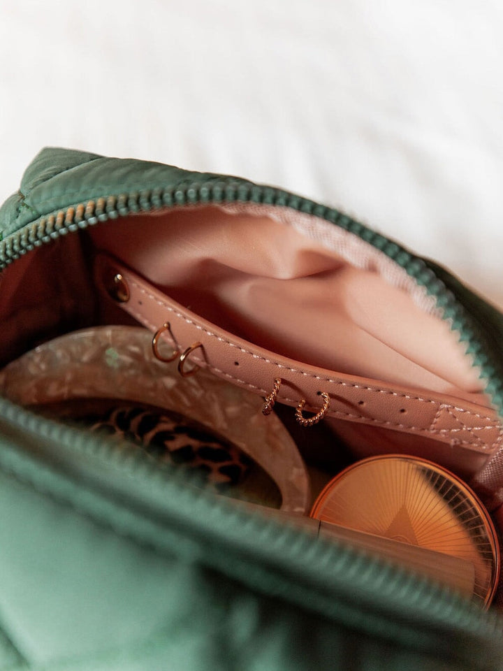 Green make up bag with pink interior containing jewelry and a compact mirror.