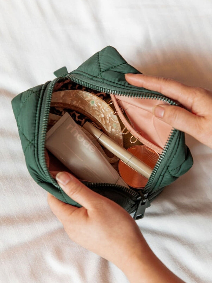 Green quilted makeup bag with cosmetic items on a white background
