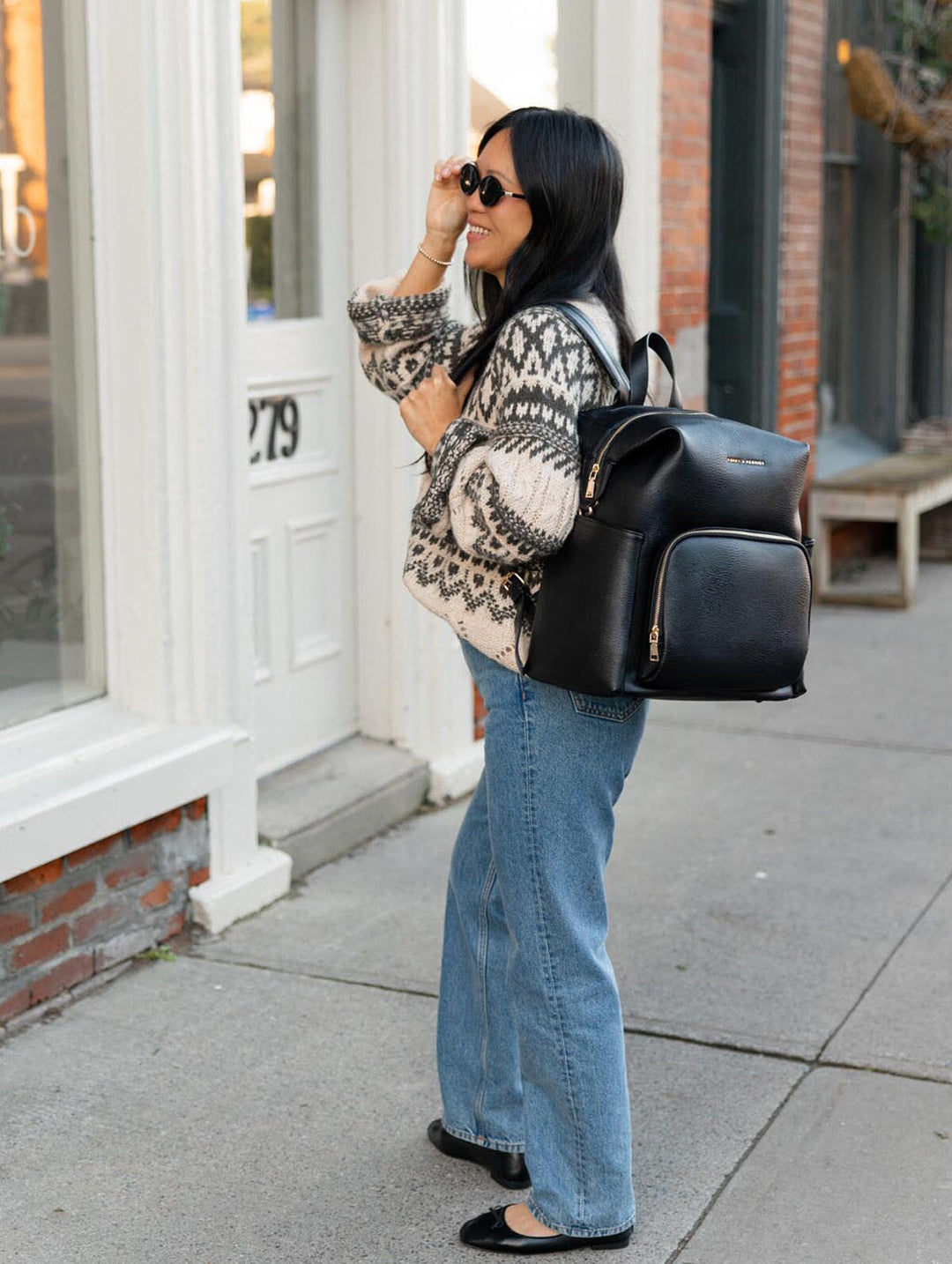 Poppy & Peonies The Cabin Backpack in Black, side lifestyle view showing the structured backpack and front zippered pocket as a woman walks along a sidewalk.