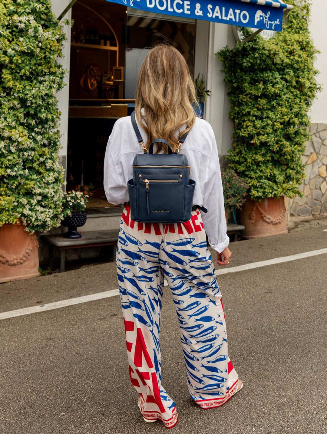 Woman wearing a blue backpack, standing in front of a Dolce & Salato store.