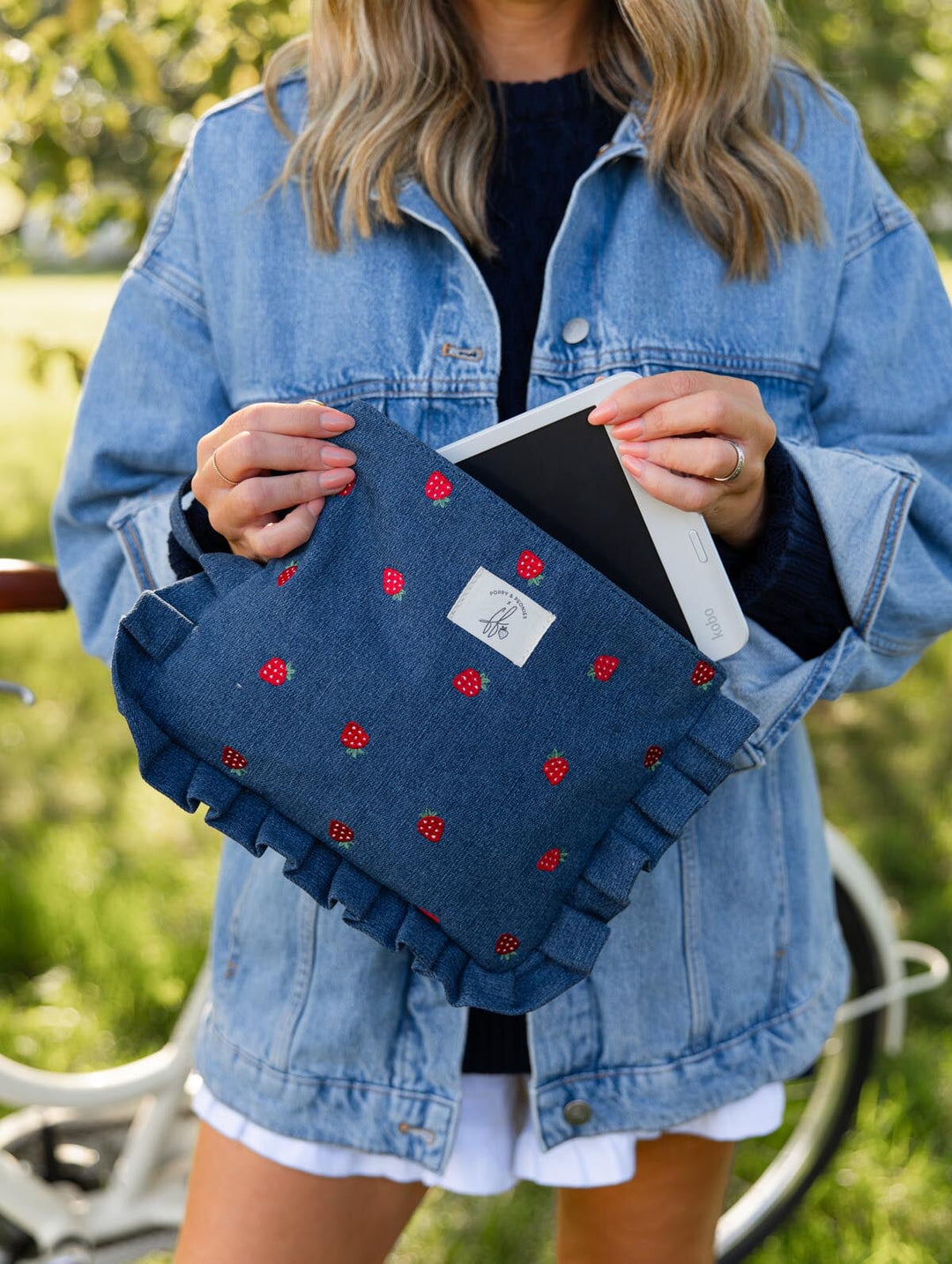 Poppy & Peonies 2-Piece Darling Ruffle Set in Strawberry Denim lifestyle view, featuring the ruffled strawberry-print pouch held open with an e-reader tucked inside.