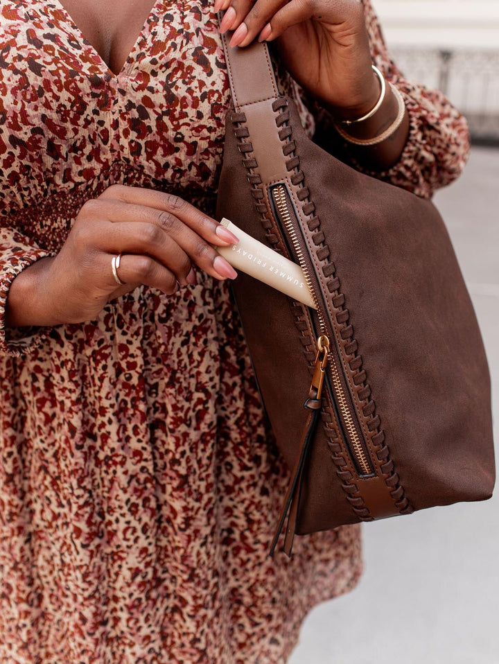 Person pulling a lip balm out of a brown vegan suede handbag.