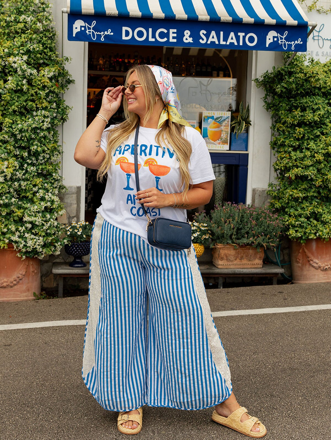 Woman in a white t-shirt with blue striped pants wearing a navy blue crossbody bag. 