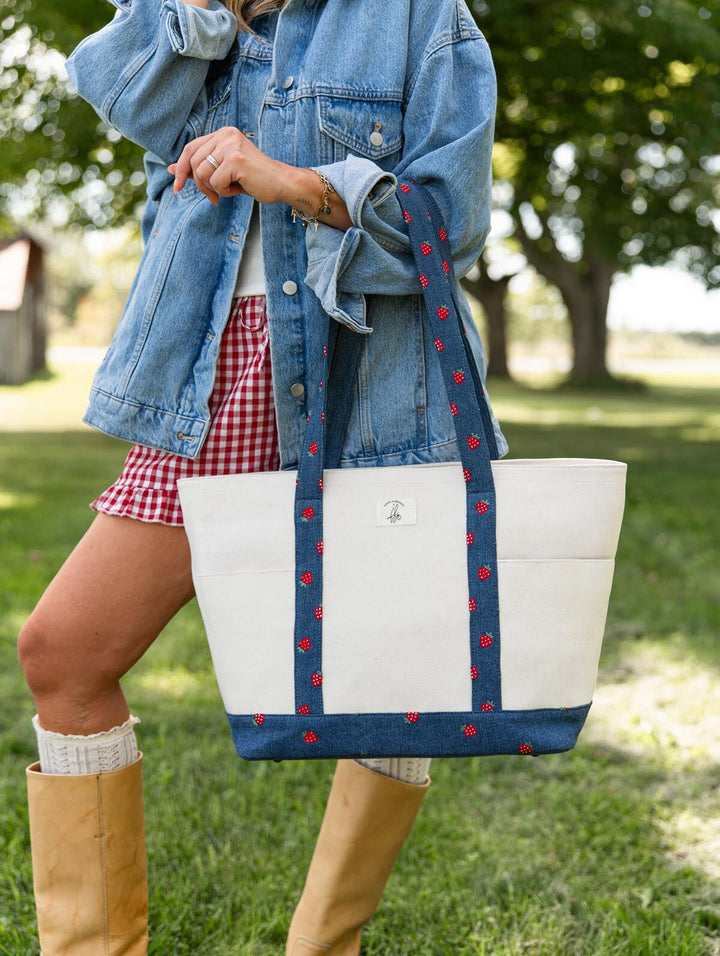 Poppy & Peonies Analog Tote in Strawberry Denim front lifestyle view, showing the roomy canvas tote with long strawberry-print denim shoulder straps and exterior slip pockets.