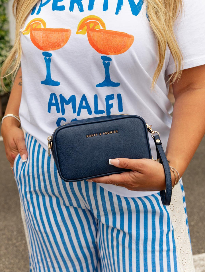 Person wearing a white t-shirt with colorful graphics and striped pants, holding a navy handbag.