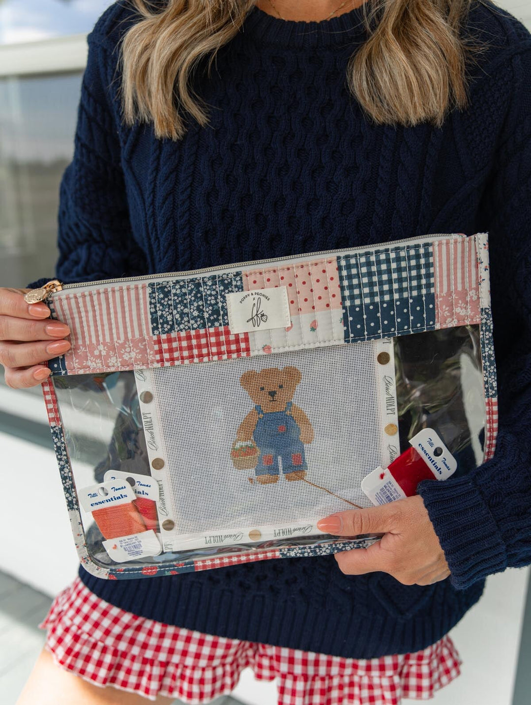 Poppy & Peonies She’s a WIP Bag in Strawberry Patchwork lifestyle view, held with a needlepoint project and embroidery thread visible through the clear front panel.