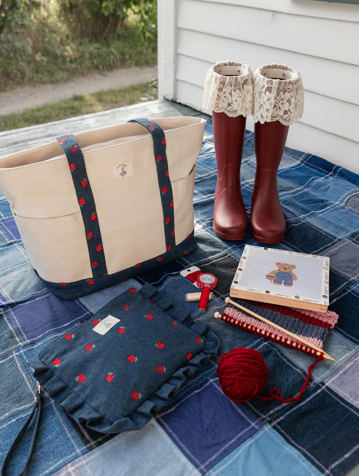 Poppy & Peonies 2-Piece Darling Ruffle Set in Strawberry Denim styled with the Analog Tote, featuring a denim-look strawberry print, ruffled edges and wrist strap alongside knitting essentials.