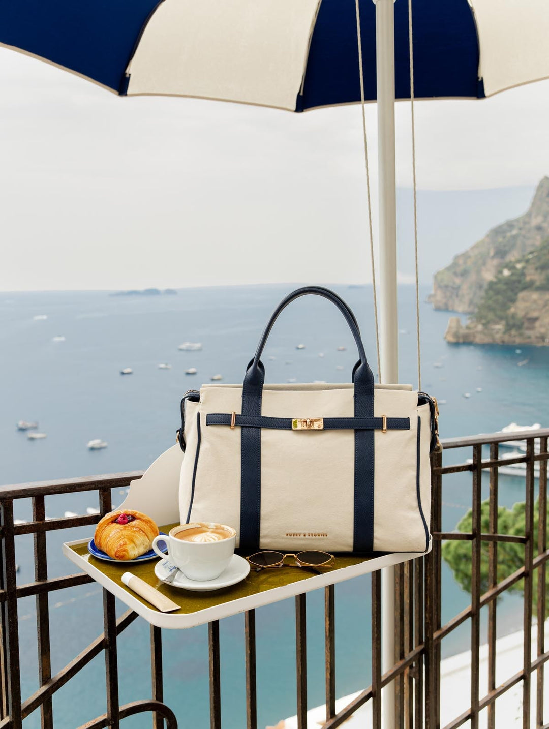 Handbag on a table with coffee and pastries, overlooking a scenic ocean view.