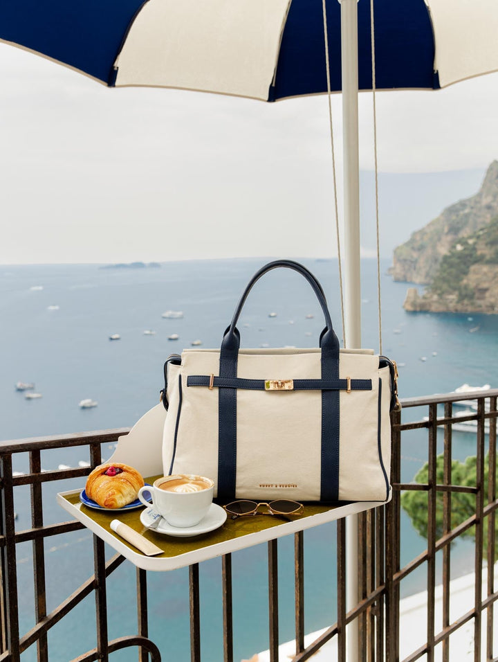 Handbag on a table with coffee and pastries, overlooking a scenic ocean view.