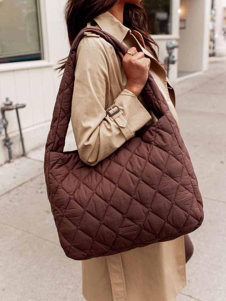 Person holding a brown quilted handbag on a city street