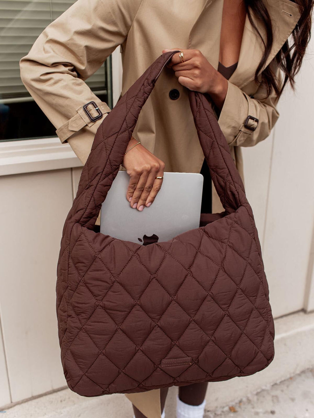 Person holding a brown quilted handbag with a beige coat.