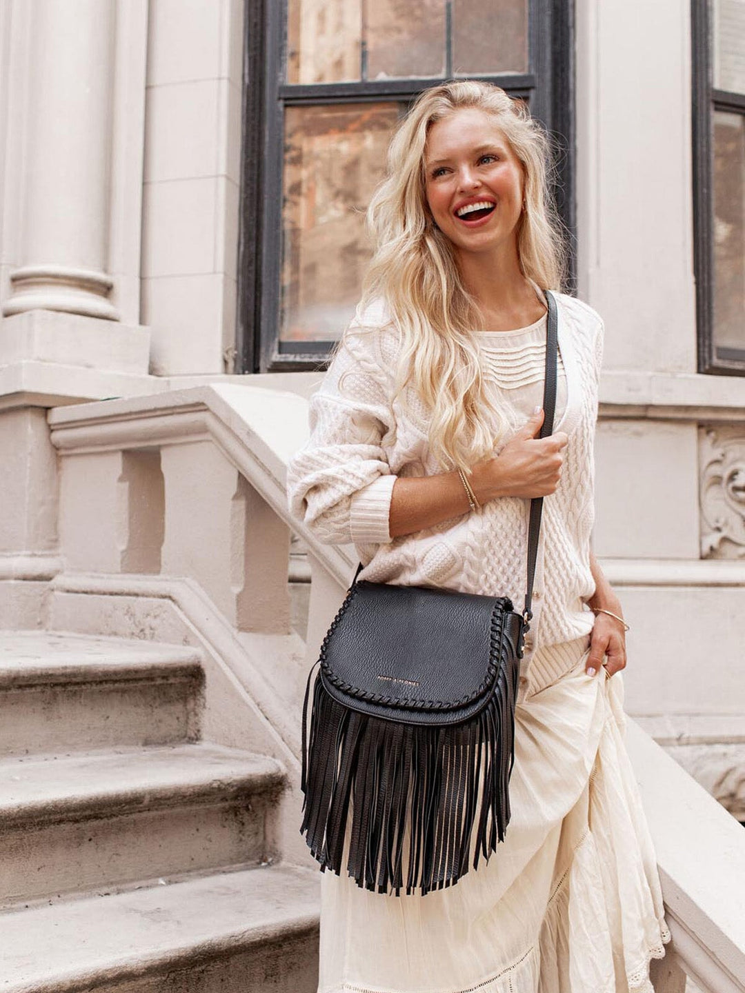 Woman holding a black fringed handbag on a city street.