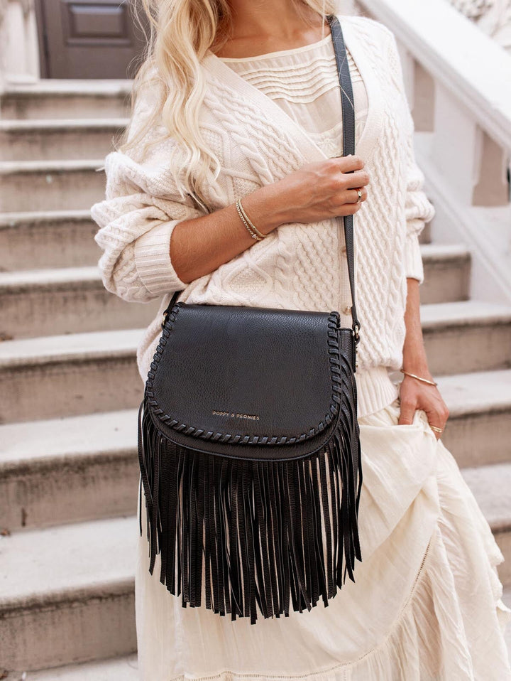 Person wearing a white sweater and holding a black fringed handbag on steps.