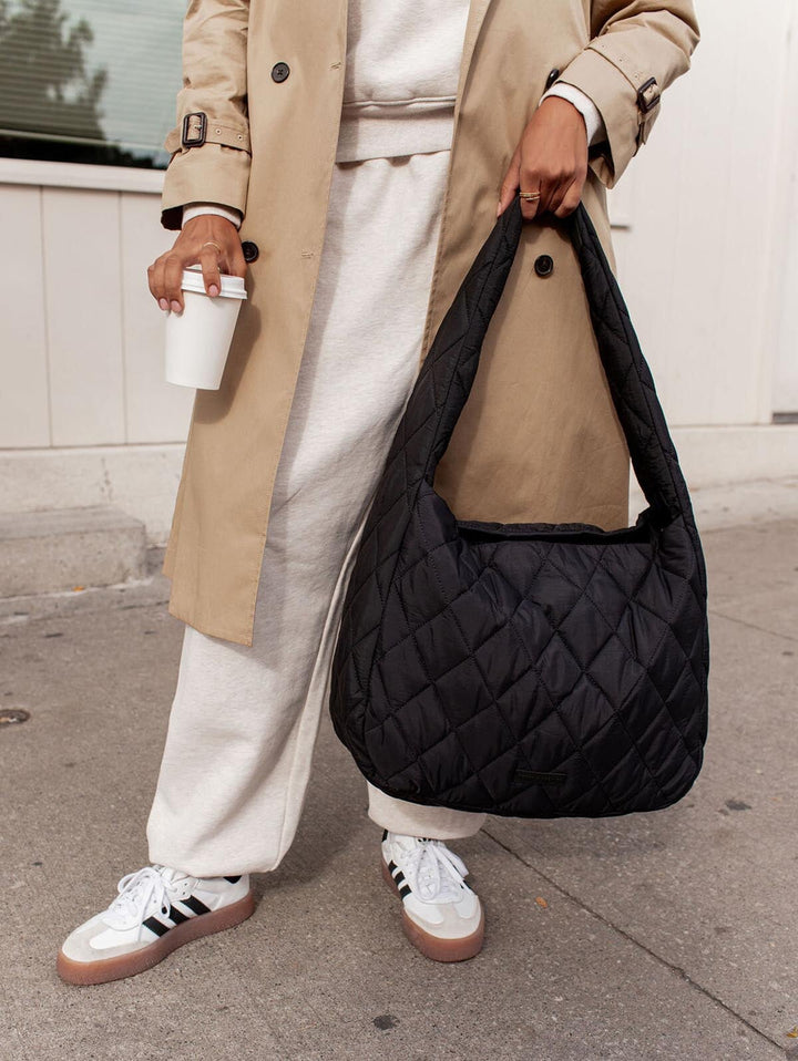 Person holding a black quilted handbag on a sidewalk
