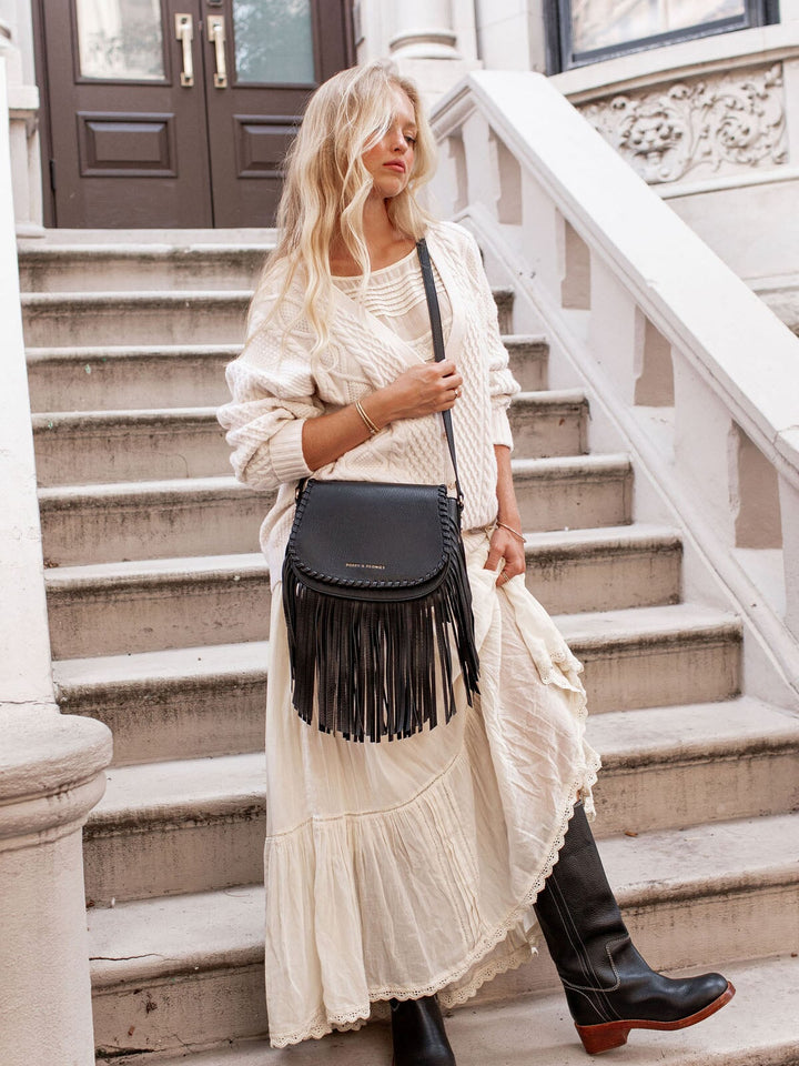 Woman in a white outfit with a black fringed bag standing on steps.