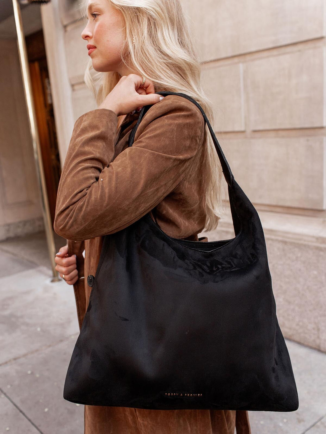 Woman carrying a black vegan suede shoulder bag in an urban setting