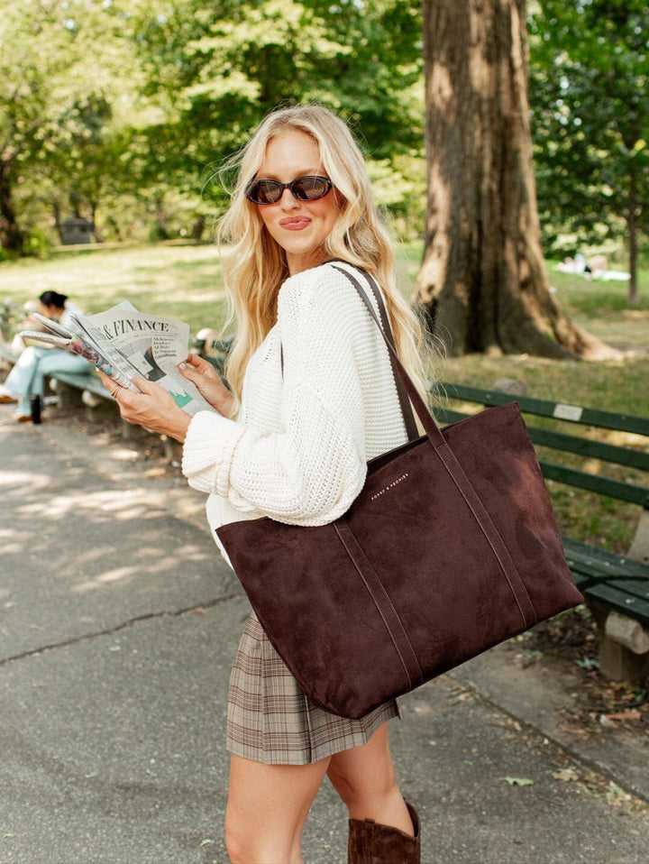 Woman holding a brown tote bag and a newspaper in a park