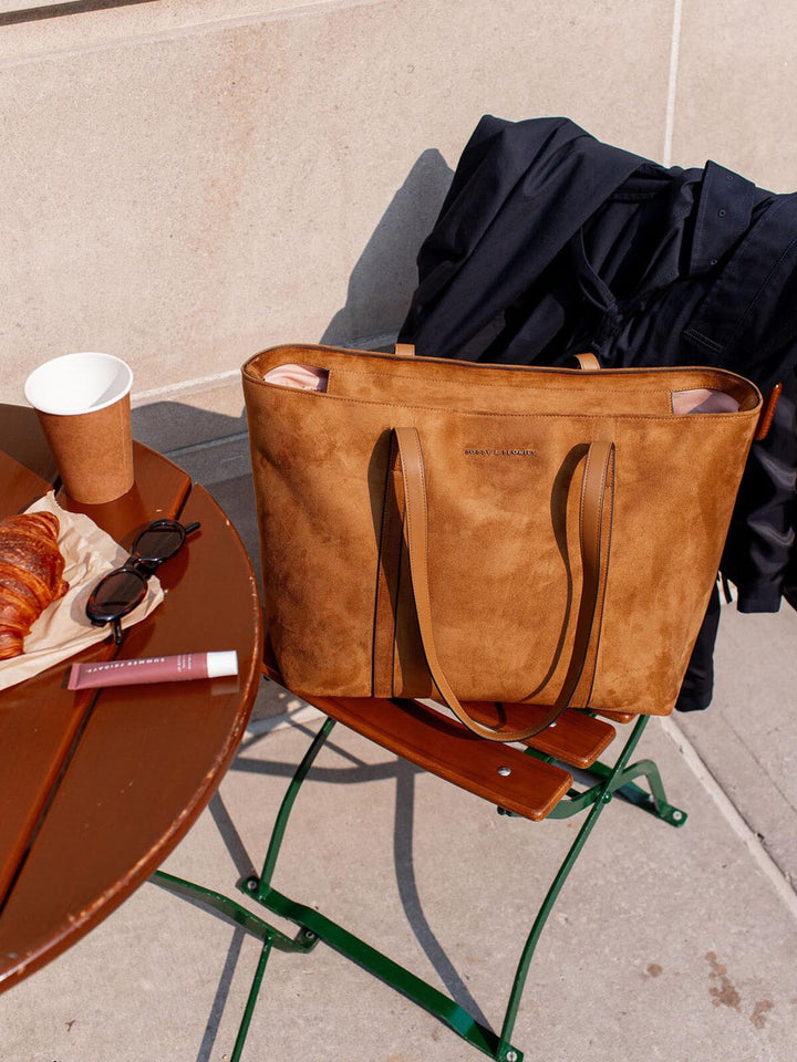 Brown vegan suede tote bag on a chair with a cup and pastries on a table outdoors.