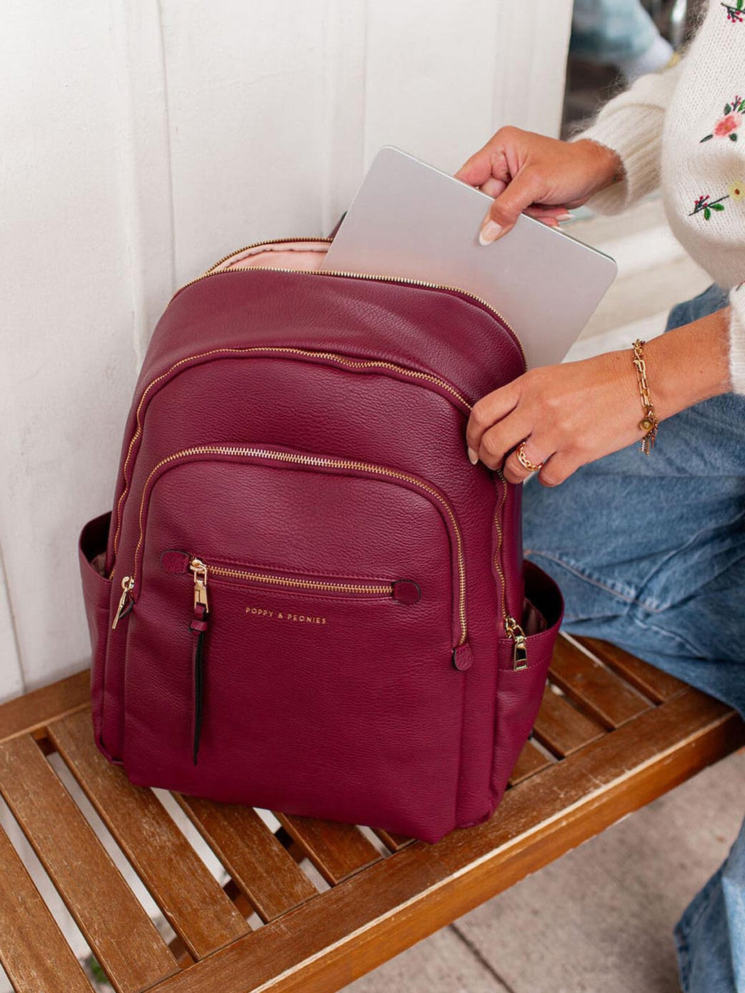 Berry coloured backpack with gold zippers on a wooden bench
