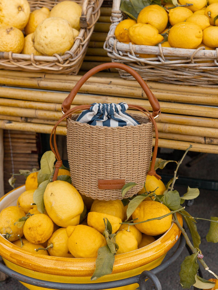Woven handbag with leather handle and strap on a bowl of lemons